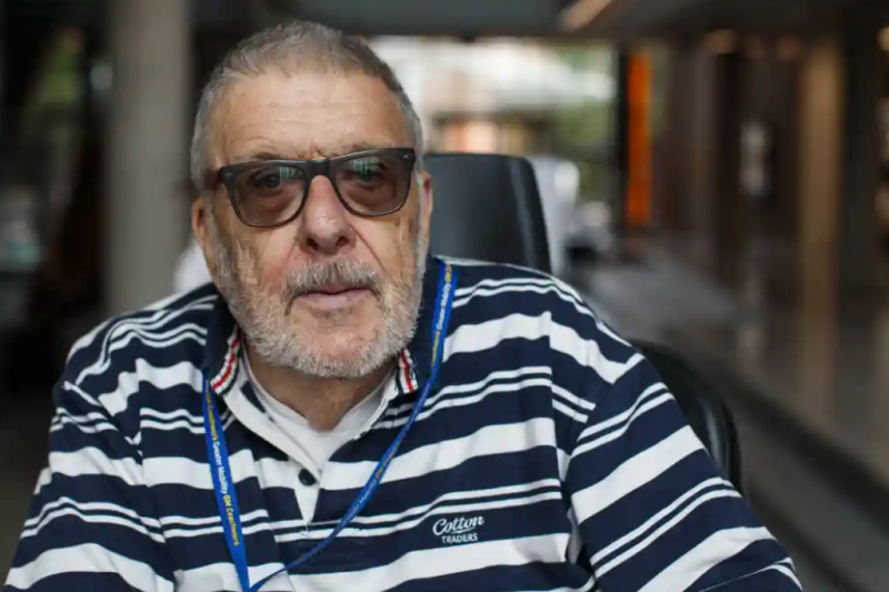 Man with sunglasses, striped top and short grey hair and beard sitting in wheelchair.