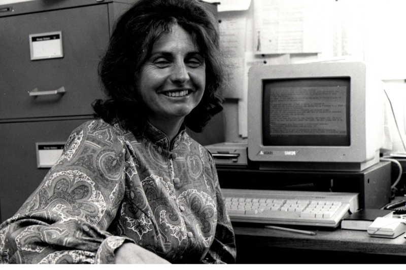Archive photo. Woman facing camera, sat at desk with old computer.